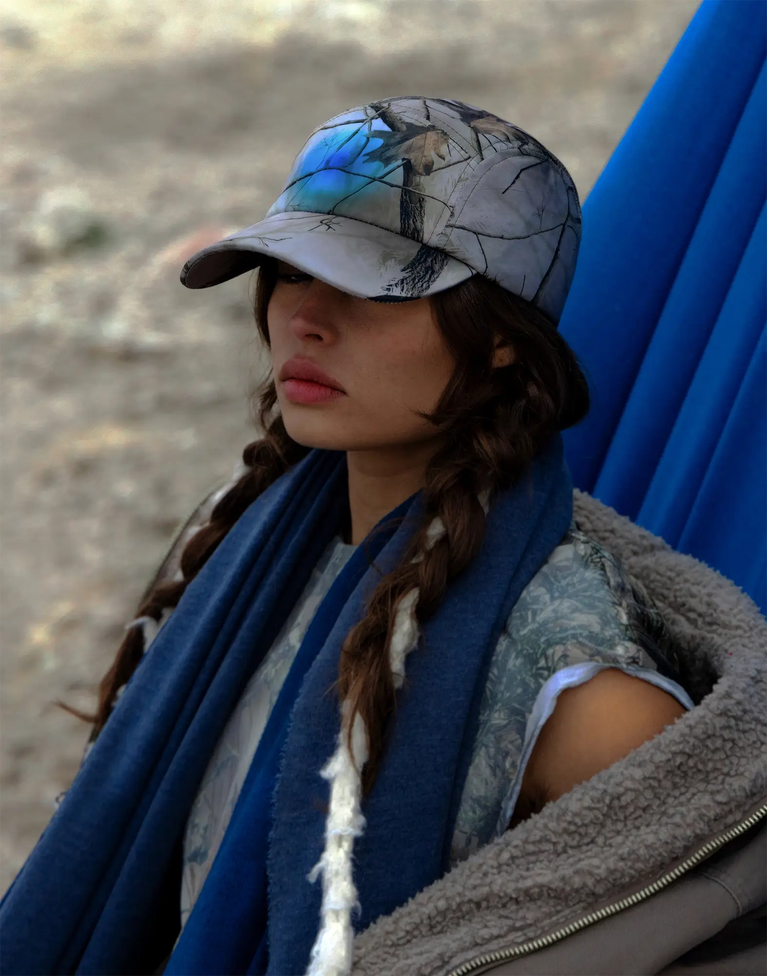 Person wearing a camouflage cap and blue scarf in a desert-like setting